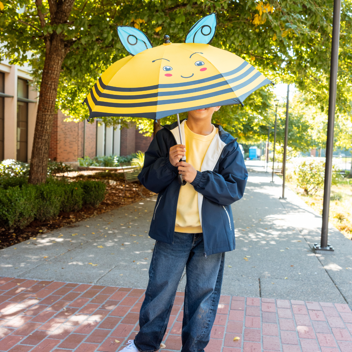Person holding a yellow and blue striped umbrella with a smiley face on a sidewalk.