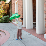 Child holding a green frog-shaped umbrella outdoors on a sidewalk.