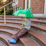 Person sitting on steps holding a green frog-shaped umbrella