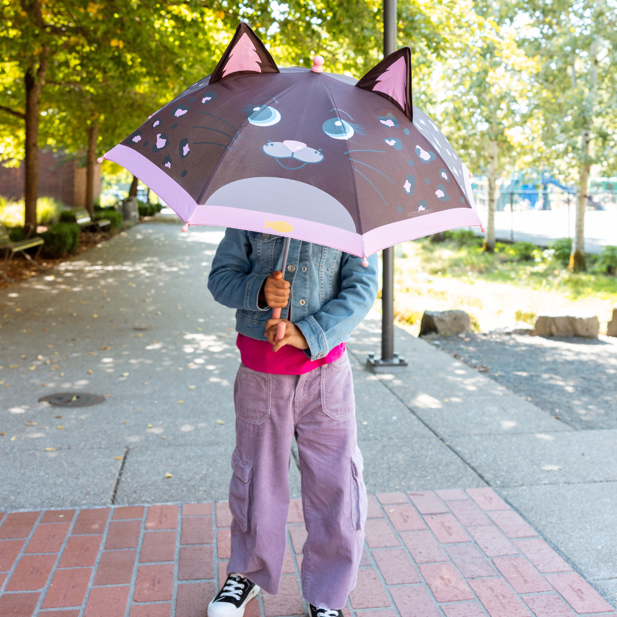 Child holding a Marcella Marcella cat-themed umbrella on a sidewalk
