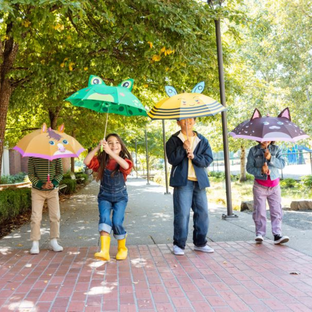 Four children with colorful umbrellas on a sidewalk in a park.