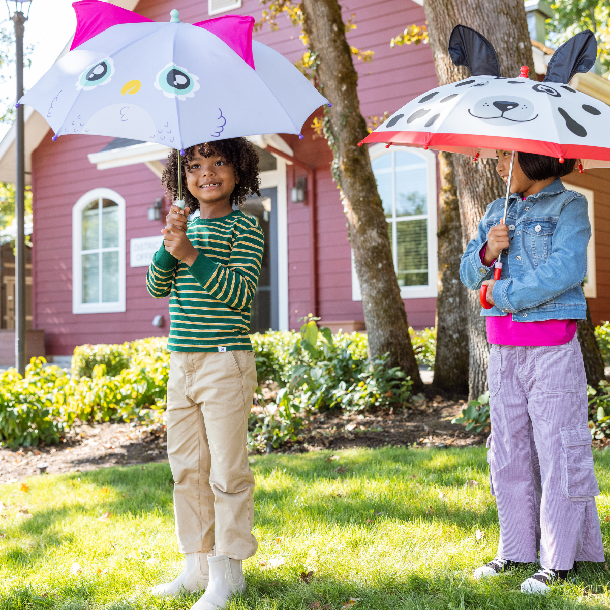 Two children holding umbrellas with animal designs in a garden setting.