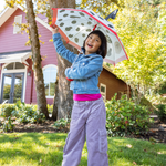 Child holding a puppy themed umbrella in a garden setting with a colorful house in the background