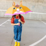 Child holding a cartoonish pony umbrella with animal ears on a concrete surface.