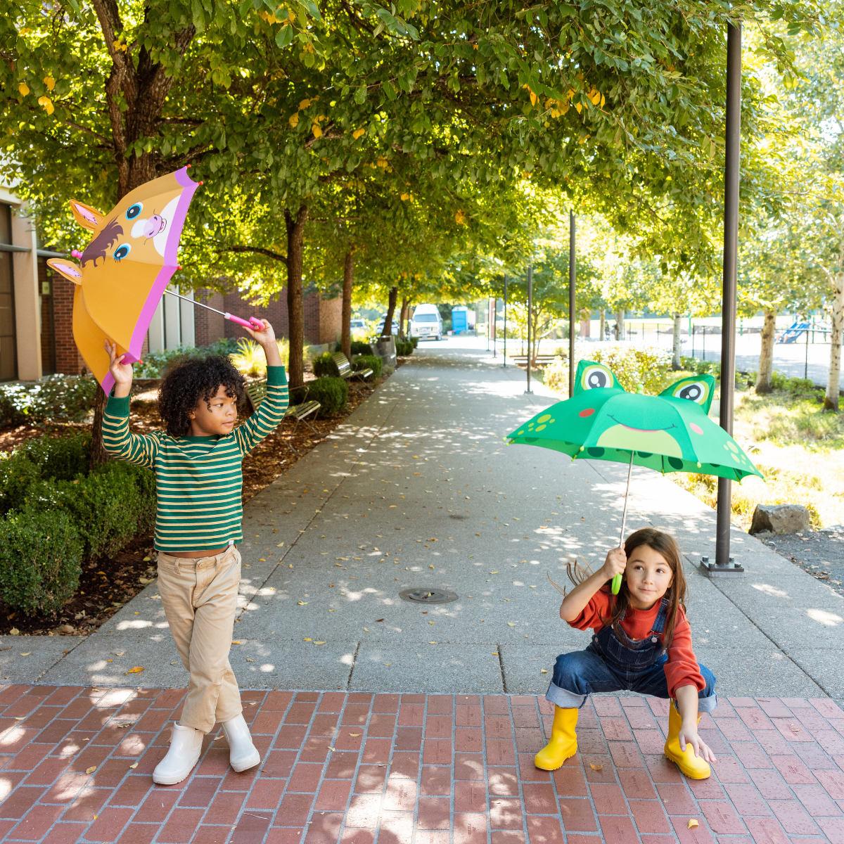Two children playing with colorful kites on a sidewalk under a tree.